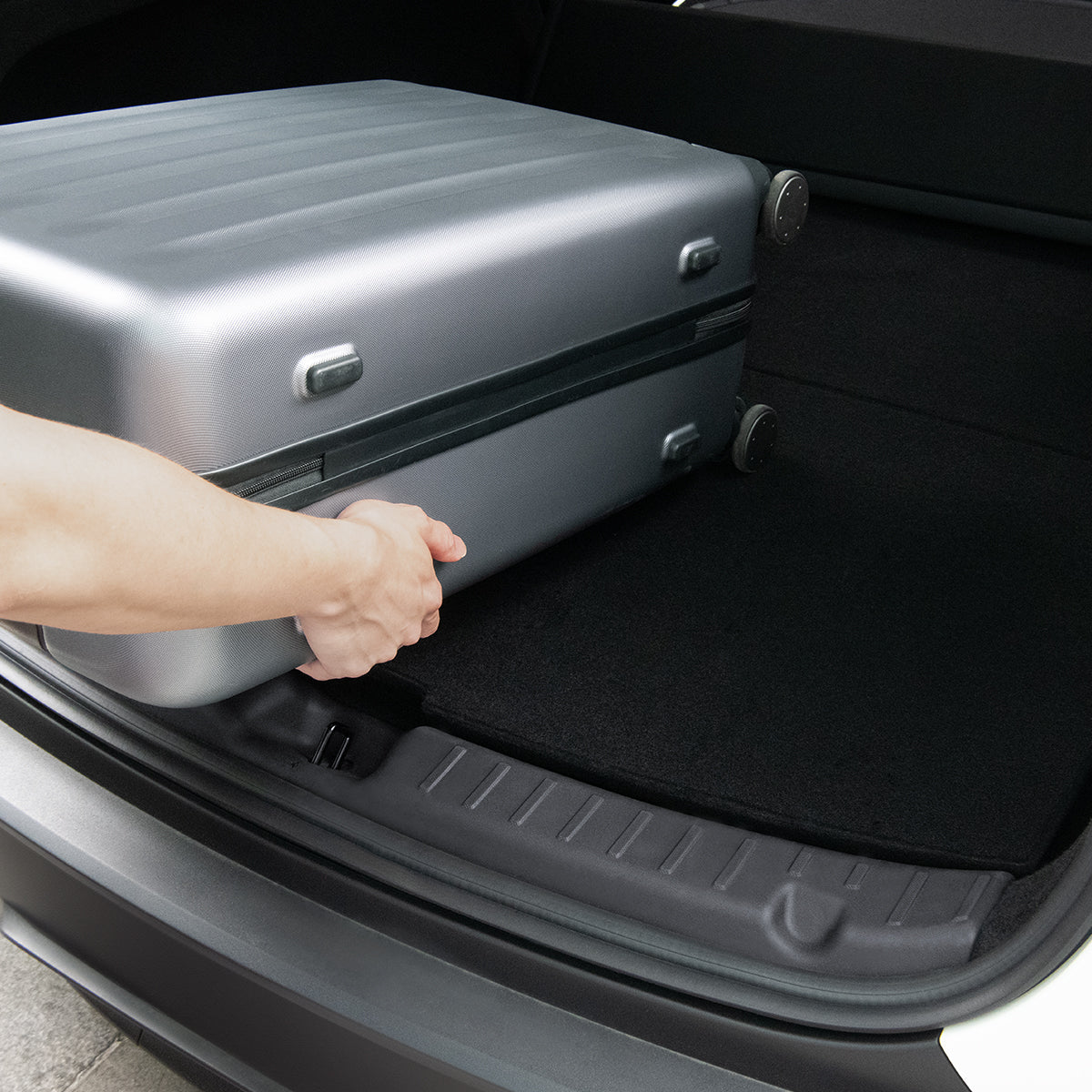 ACP09759 - Tesla Model Y Juniper Trunk Sill Guard | TG100-YJ in black showing someone placing luggage and the guard protecting the trunk